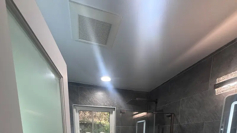 Remodelled bathroom with dark tile, glass shower and backlit mirror
